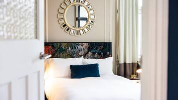 A hotel room with a bed, a round mirror, and a floral headboard.