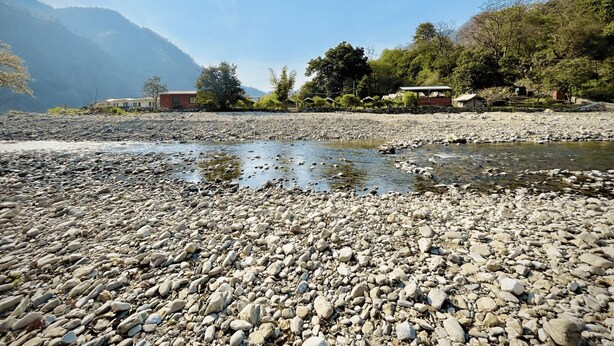 A rocky riverbed with a clear sky and mountains in the background. - Riverstone Camps and Resorts (Yamkeshwar)