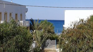 A coastal view with a white building, a fenced area, and dense foliage. - Milos Apartments  (Faistos)