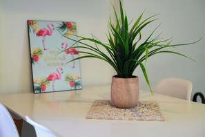 A table with a potted plant, a decorative plate, and a painting with flamingos. - Milos Apartments  (Faistos)