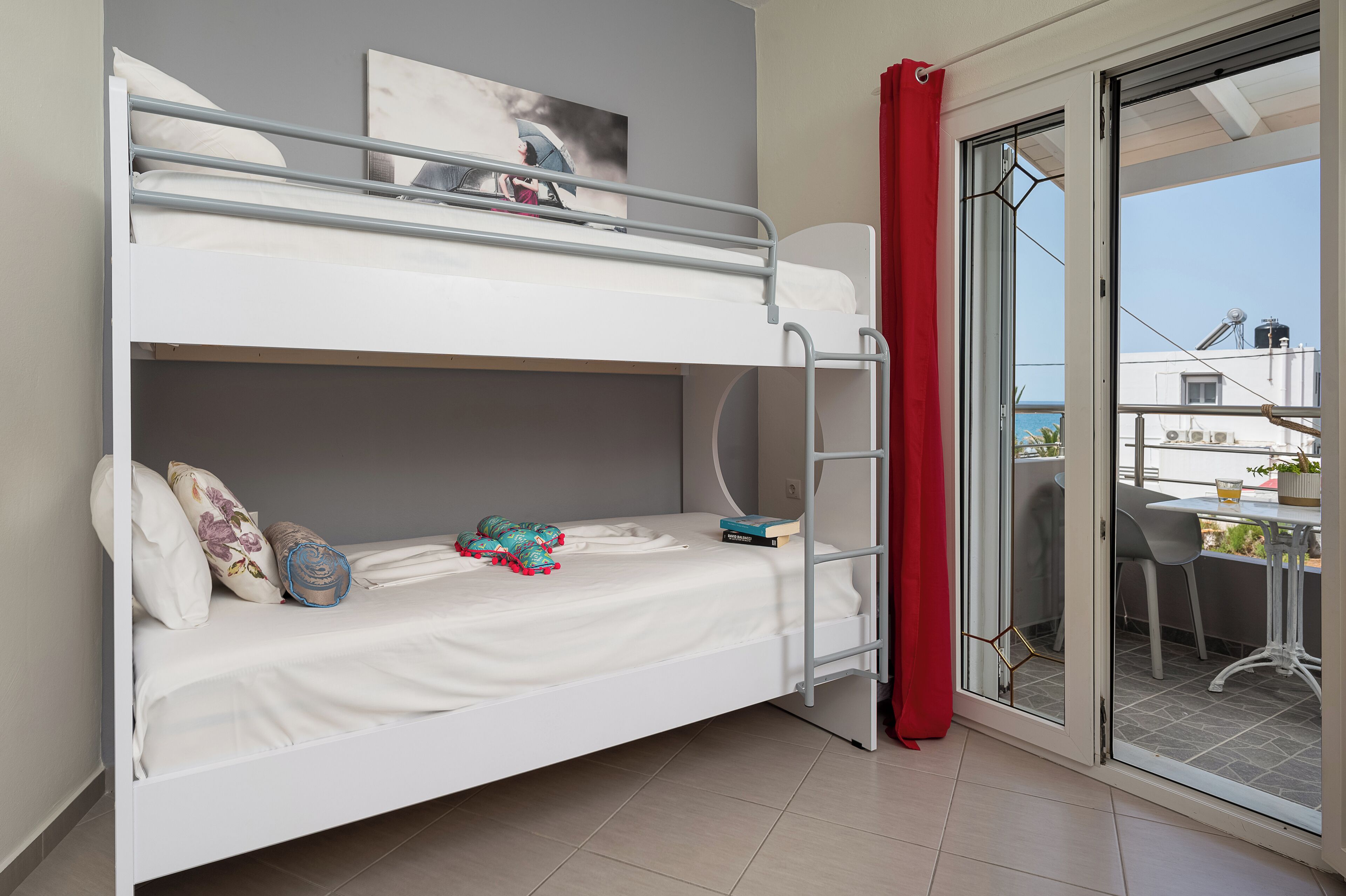 Una cama individual superpuesta con escalera, una cortina roja y vistas al exterior a través de un ventanal.