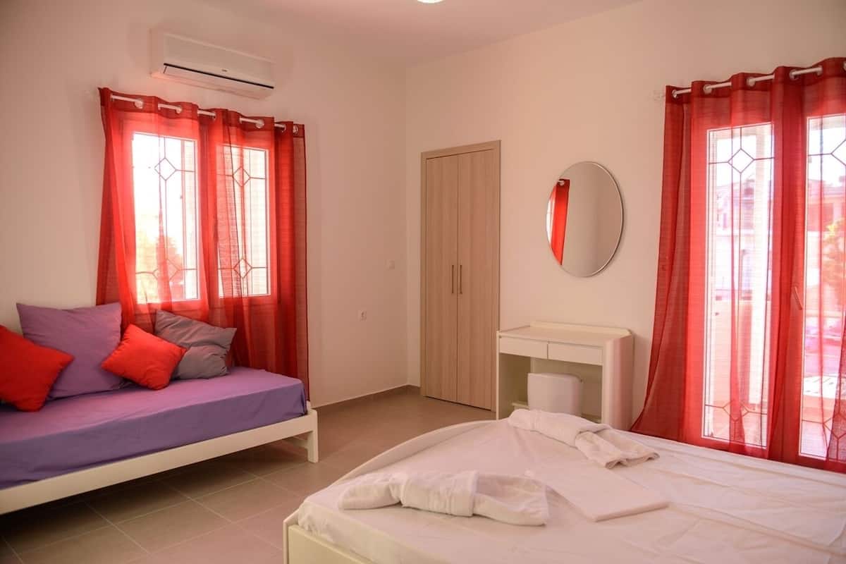 A bedroom with two beds, a wardrobe, a mirror, and a window with red curtains.