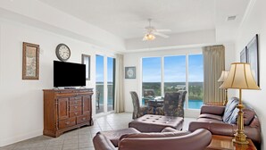 A spacious living room with a flat-screen TV, leather furniture, and a balcony with a view. - Waterfront 2BR at The Wharf • Sleeps 6 • Amazing Views • Oasis Pool (Orange Beach)