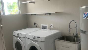A laundry room with two front-loading washing machines, a small sink, and a cabinet.