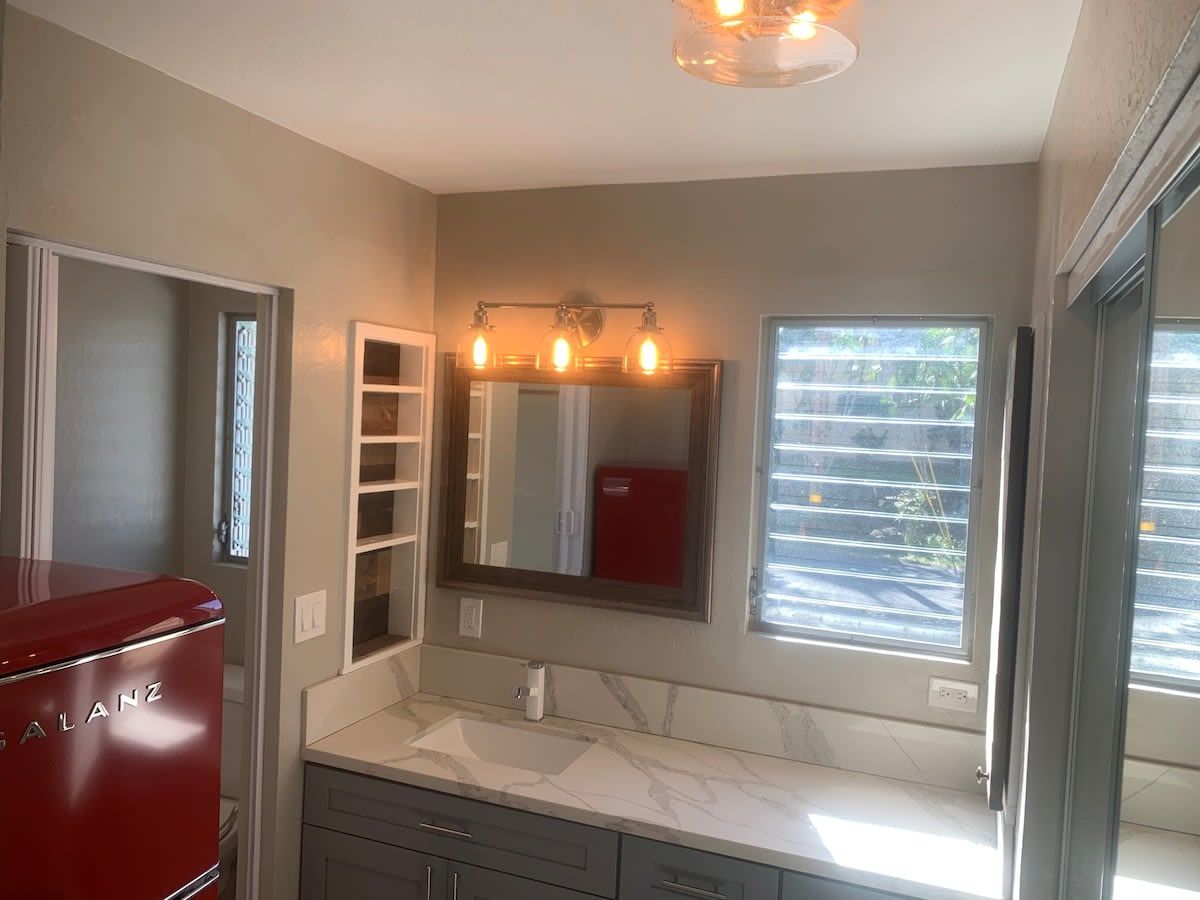 A bathroom with a red appliance, a sink, a mirror, and a window.