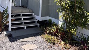 Una casa con porche cubierto, escalones que conducen a la entrada y un pequeño jardín con diversas plantas.