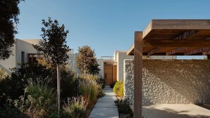 A modern architectural structure with a stone wall, a wooden pergola, and a pathway leading to a wooden door.