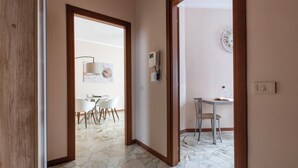 A hallway with a dining area visible through an open door. There is a dining table with chairs, a wall-mounted air conditioning unit, and a wall clock. - Italianway - Campania 26 A (Milan)