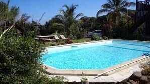 A rectangular swimming pool with clear blue water, surrounded by rocks and greenery. - Gite Perroquets, 2 Chambres, Calme, vue mer (Sainte-Rose)