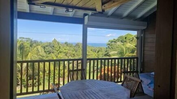 A balcony with a bed and a view of the ocean and greenery. - Gite Perroquets, 2 Chambres, Calme, vue mer (Sainte-Rose)