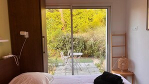 Ein Schlafzimmer mit Bett, Nachttisch, Steckdose und Blick auf einen Garten durch eine Schiebetür.