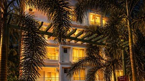 Un hôtel à plusieurs étages, avec une allée pavée en briques et des palmiers.