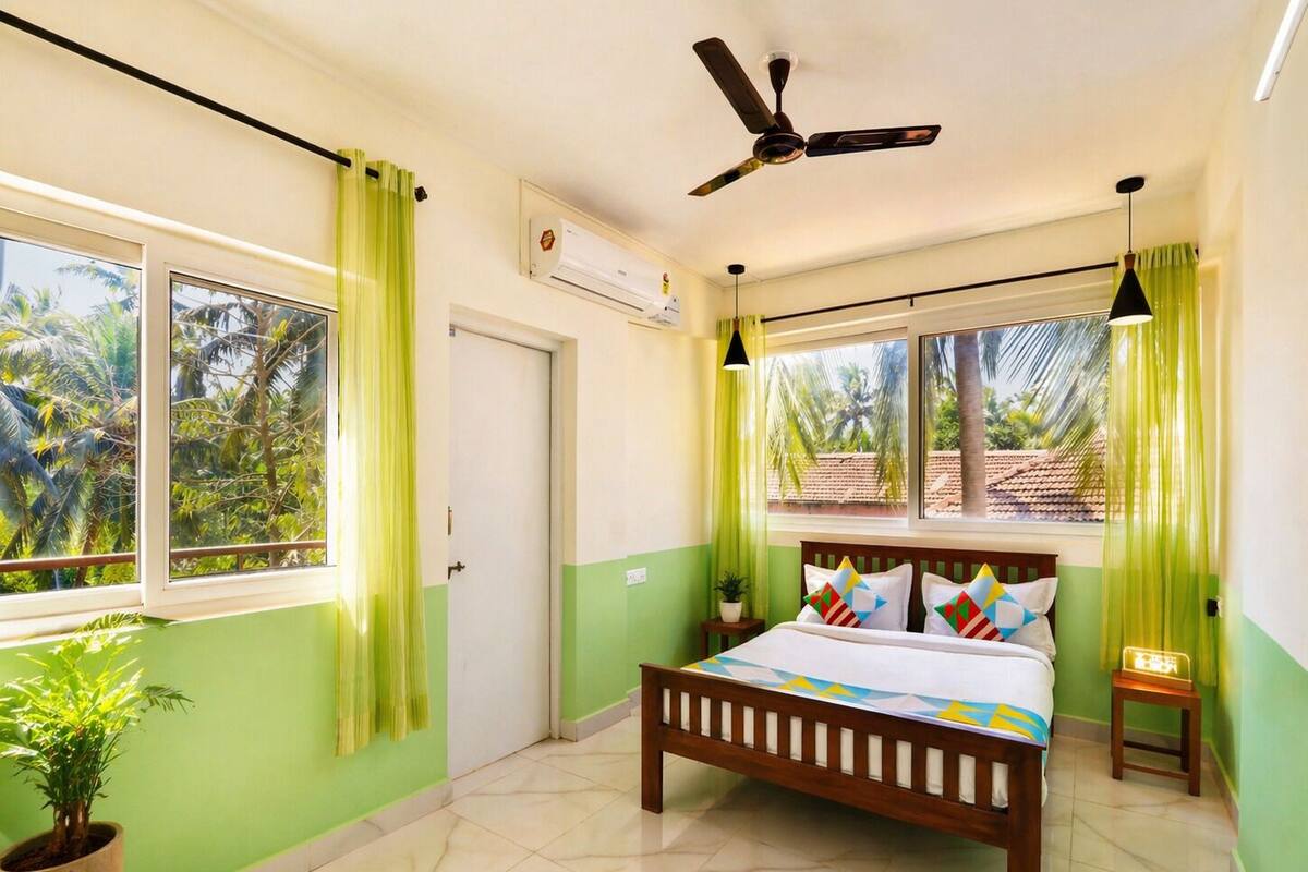 A bedroom with a bed, a ceiling fan, a window with curtains, a potted plant, and a small bedside table.
