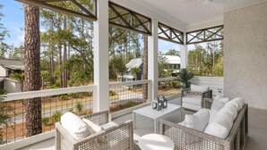 A covered outdoor seating area with wicker furniture and a view of the surrounding forest. - Poolside Privacy & Dining Under the Stars (Bluffton)