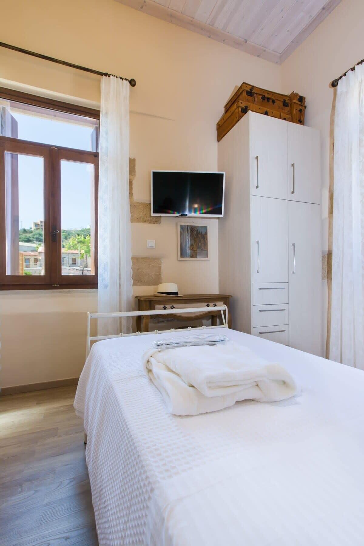 Ein Schlafzimmer mit einem Bett, einem Fernseher, einem Kleiderschrank und einem Fenster mit Vorhängen.