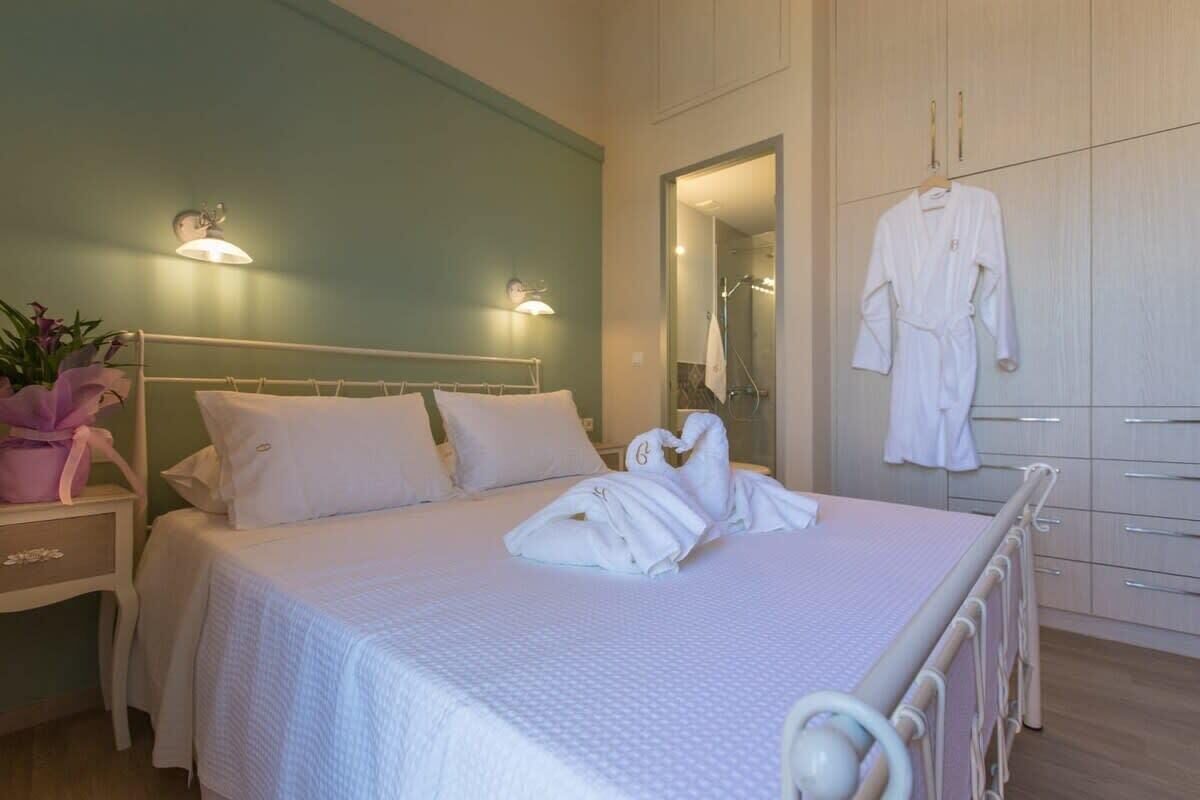 A neatly made bed with white linens, a bedside table with a pink flower vase, and a white robe hanging on a rack.
