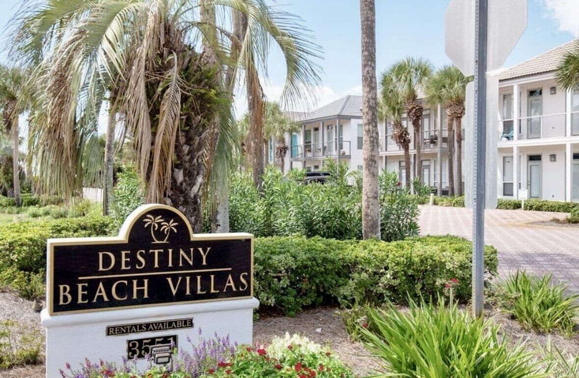 Une enseigne indiquant l’emplacement de Destiny Beach Villas, avec un jardin tropical et des bâtiments en arrière-plan.