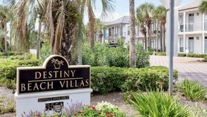 A sign for Destiny Beach Villas with a tropical garden and buildings in the background. - Waterfront Villa*Steps to Beach*Pool*King Beds (Destin)