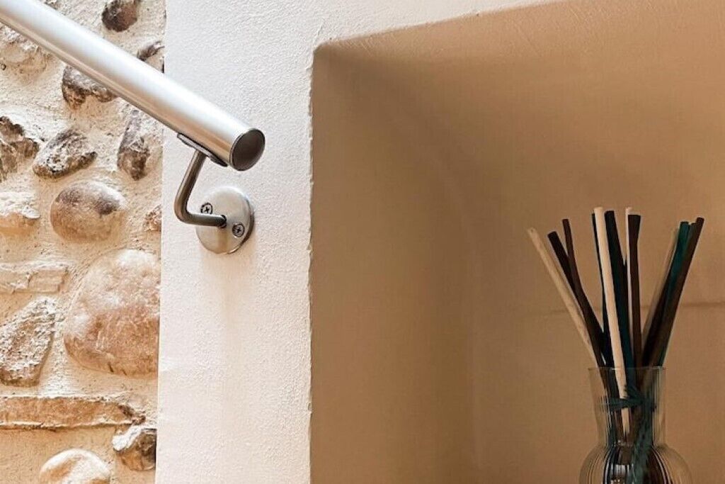 Un muro de piedra, una barandilla metálica y un florero de vidrio con cañas.