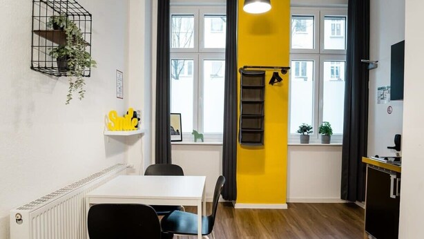 A modern kitchen with a white countertop, black chairs, and a yellow accent wall. - Cosy Box @ Boxhagener Platz (Berlin)