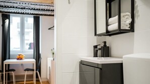 Une salle de bain moderne avec un lavabo blanc, un meuble noir et un porte-serviettes sur lequel sont pliées des serviettes.
