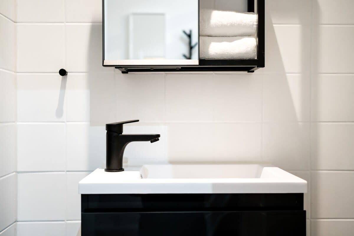 Ein modernes Badezimmer mit einem weißen Waschbecken, einem schwarzen Wasserhahn und einem Spiegel darüber.