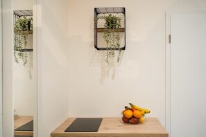 A room with a wooden table, a black tablet, and a fruit bowl. There are two black metal wall shelves with plants. - Cosy Box @ Boxhagener Platz (Berlin)