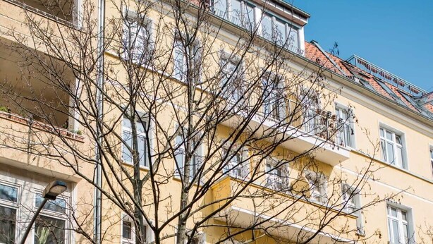 A multi-story yellow building with balconies, a tree in front, and parked cars. - Cosy Box @ Boxhagener Platz (Berlin)