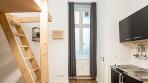 A kitchen with a wooden ladder, a window with curtains, and a black cabinet. - Cosy Box @ Boxhagener Platz (Berlin)