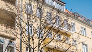 A multi-story yellow building with balconies, a tree in front, and parked cars. - Cosy Box @ Boxhagener Platz (Berlin)