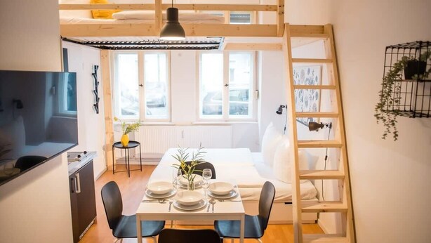 A compact, modern apartment with a loft bedroom, a dining area with a table set for four, and a kitchenette. - Cosy Box @ Boxhagener Platz (Berlin)