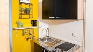 A compact kitchen with a yellow accent wall, a black cabinet, and a built-in stove. - Cosy Box at Boxhagener Platz (Berlin)