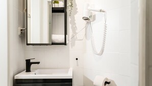 A bathroom with a white sink, black faucet, and a mirror above it. There is a towel rack with a towel and a small plant on the wall. - Cosy Box at Boxhagener Platz (Berlin)