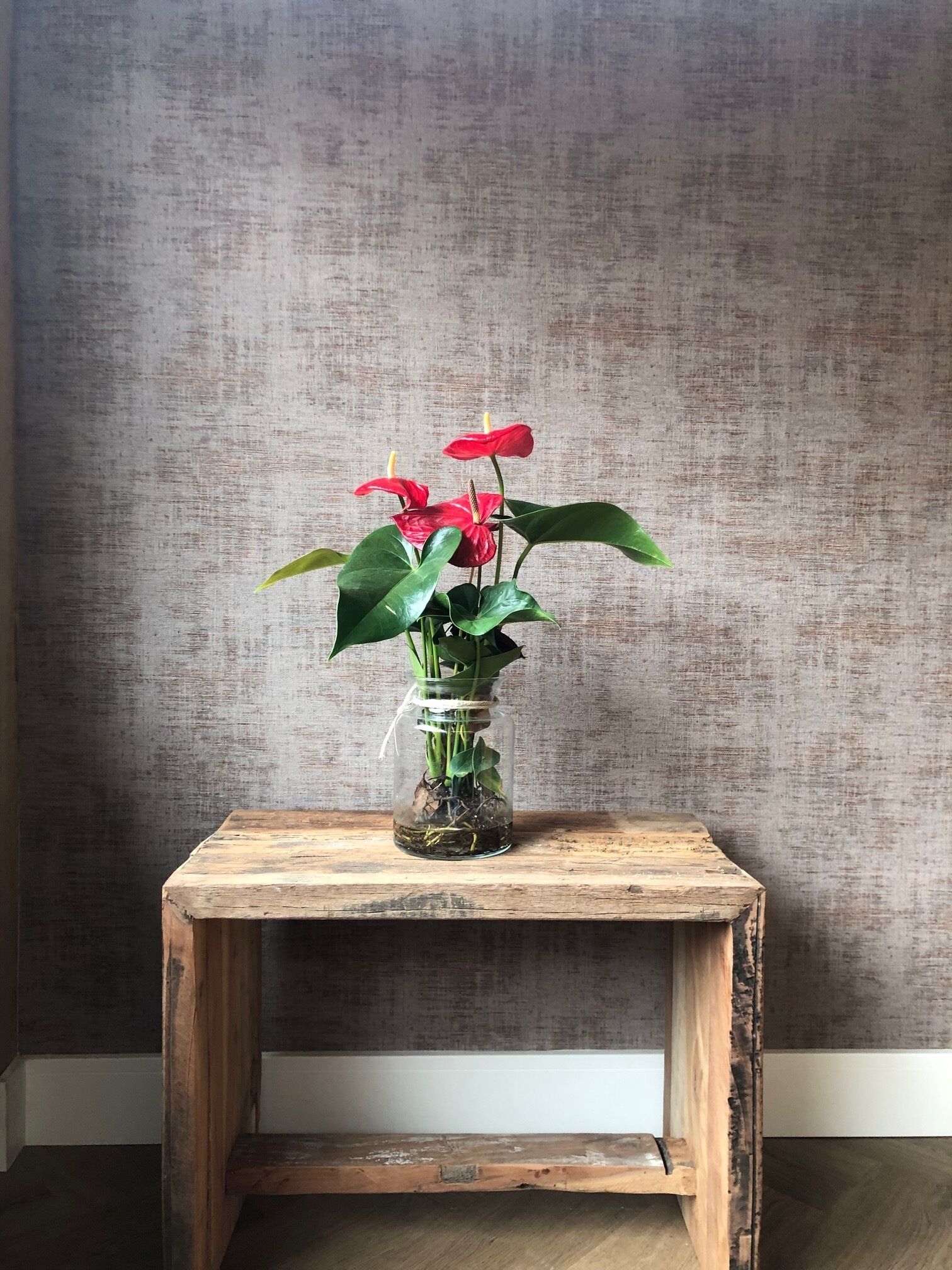 Ein kleiner Holztisch mit einer Glaskaraffe, in der rote Blumen und grüne Blätter stecken.