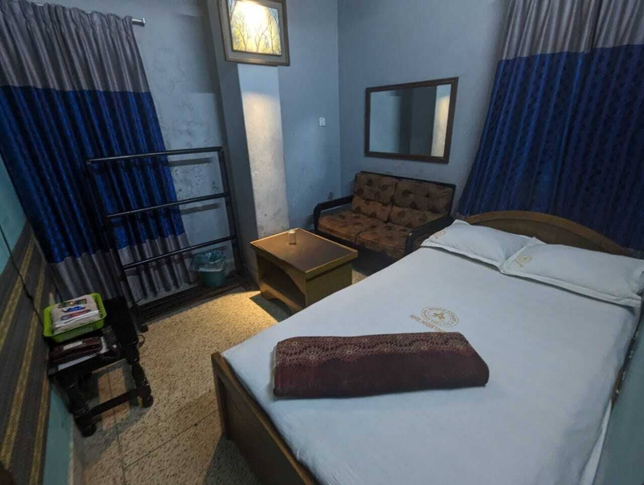 A hotel room with a bed, a small table, a chair, a mirror, and curtains.