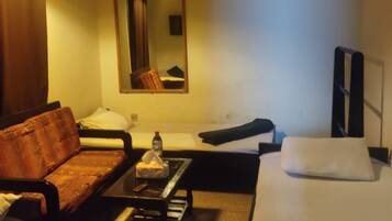 A hotel room with a sofa, a small table, a bed, a ceiling fan, a mirror, and a TV.