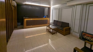 A modern reception area with a wooden reception desk, a sofa, and a TV. - Hotel Hoque Tower International (Chittagong)