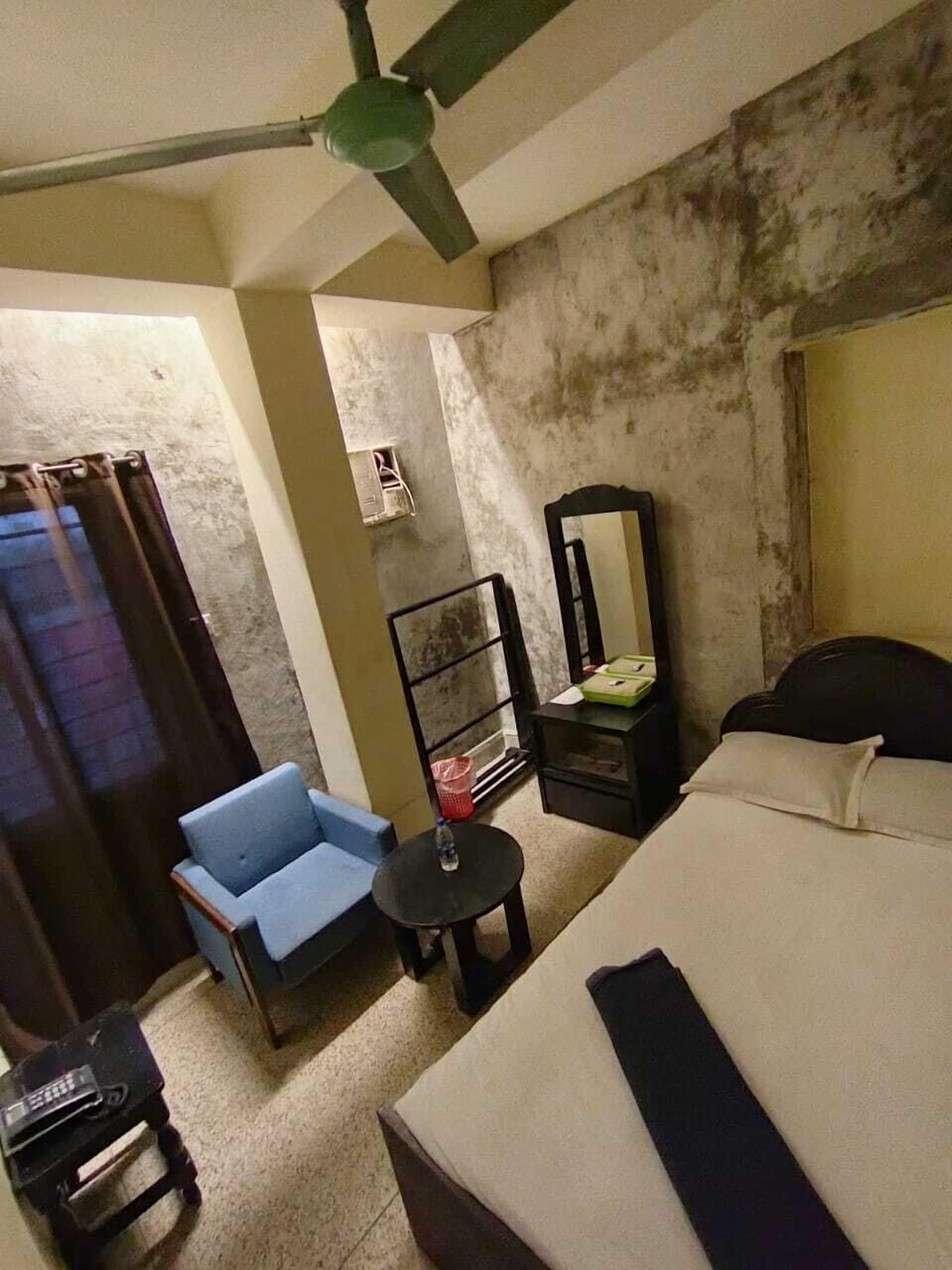 A bedroom with a bed, a chair, a small table, a mirror, and a ceiling fan.