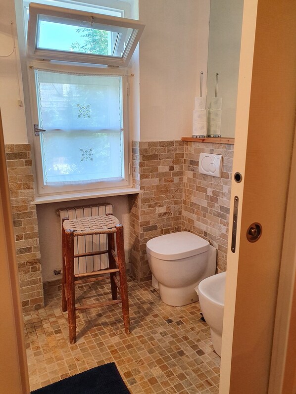 A small bathroom with a window, a toilet, and a wooden stool. - B&B Cristallo (Cortina d'Ampezzo)