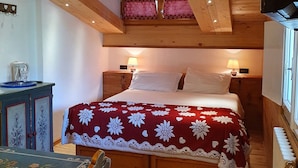 Un dormitorio acogedor de madera con una cama, dos lámparas de noche, un tocador y un televisor.