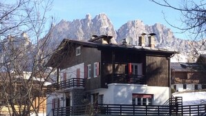 Un edificio de dos pisos con un balcón, un coche estacionado adelante y nieve en el suelo.