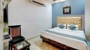 Un dormitorio con cama, una silla, una mesita, aire acondicionado y televisor de pared.
