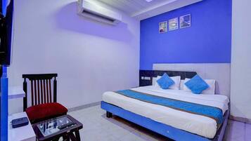 A hotel room with a bed, a chair, a table, and an air conditioning unit.
