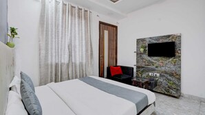 Un dormitorio con cama, televisor montado en pared de piedra, puerta de madera y una pequeña mesa con una planta.