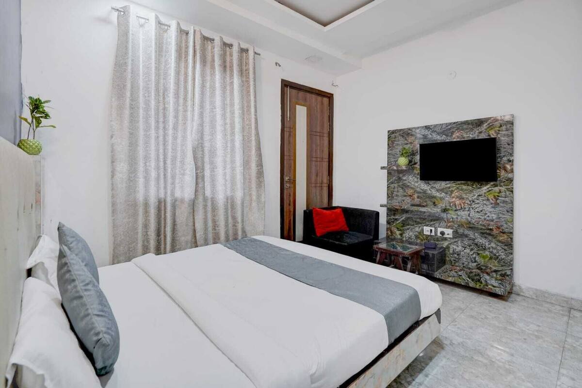 Un dormitorio con cama, televisor montado en pared de piedra, puerta de madera y una pequeña mesa con una planta.