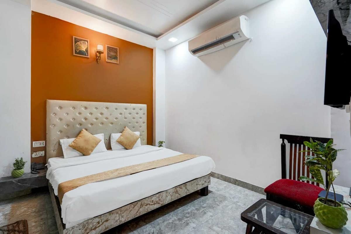 Habitación de hotel con una cama, un banco rojo, una mesita pequeña y una planta en maceta.
