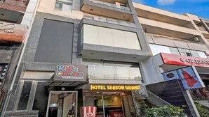 Un edificio de varios pisos con una arena de juegos y fiestas a nivel de calle llamada 'Kidz Funtale', y un hotel llamado 'Hotel Season Grand' con una entrada visible y un puesto de palomitas de maíz afuera.