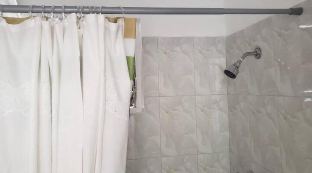 Un espacio de ducha con cortina, paredes de azulejos y un cabezal de ducha de mano.