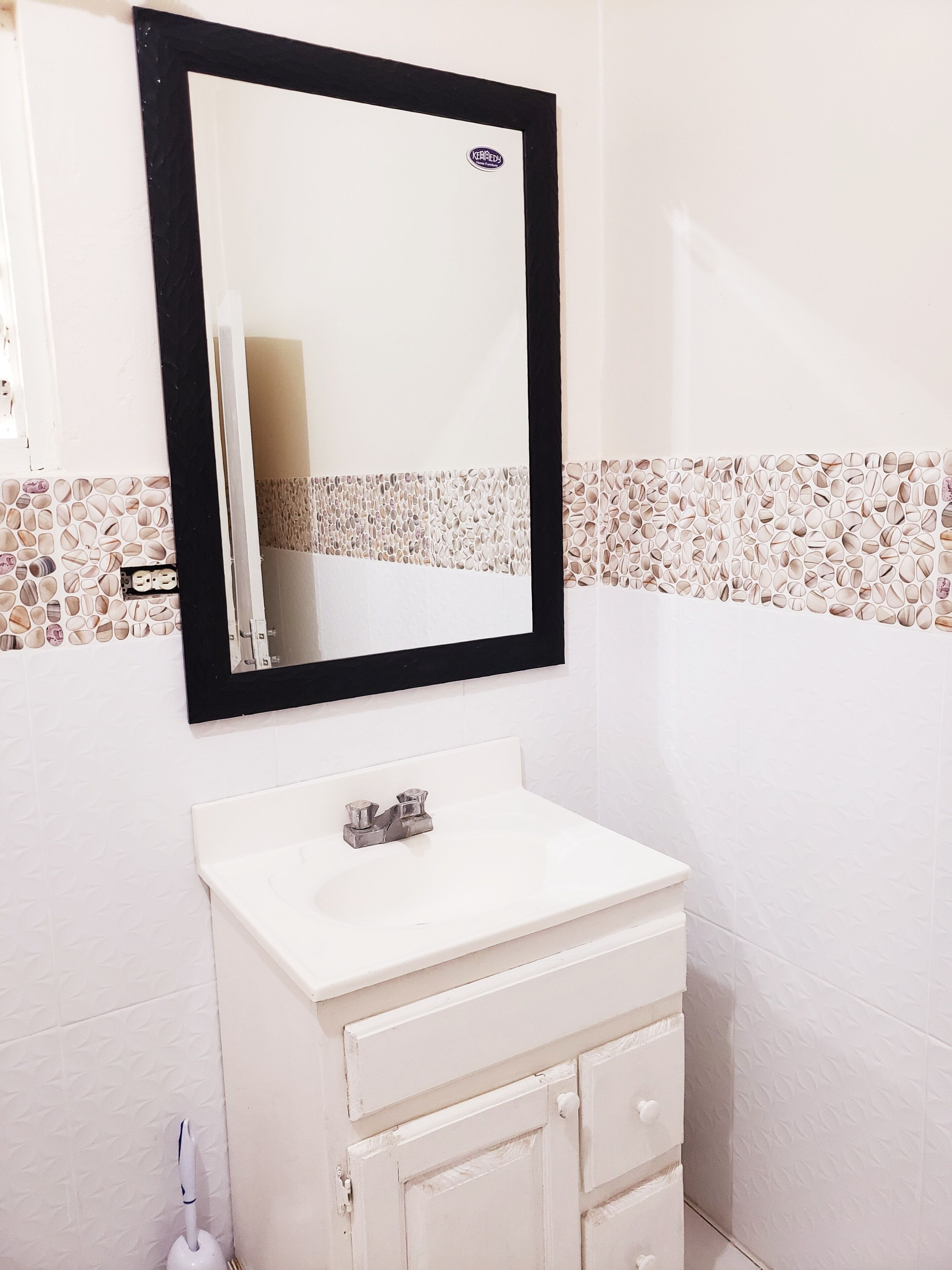 Une salle de bain avec un lavabo blanc, un miroir à cadre noir et une bordure décorative en carreaux.