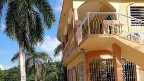 Ein Gebäude mit Balkon, Pflasterweg und einer Palme.